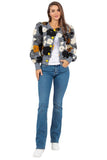 Woman wearing a floral patterned bomber jacket and blue jeans on a white background