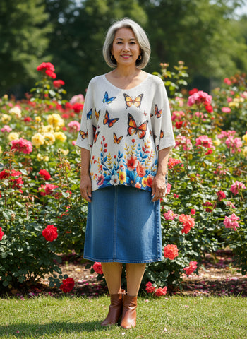 white mesh 
sweater with colorful butterfly and floral design on a hanger against a white background