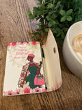 Small notebook with a floral design and illustration of a woman on a wooden surface with a cup of coffee.