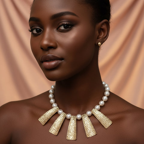 Pearl necklace with gold pendants and matching earrings on a pink background