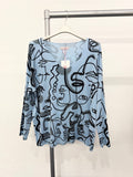 A blue lightweight knit top with an all-over abstract art print, displayed on a hanger.