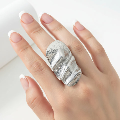 An adjustable silver ring with an irregular hammered plate design, displayed on a white surface.