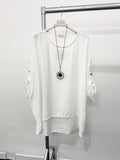 A white plus-size top with a necklace hanging on a display rack, with the top flatly displayed below.
