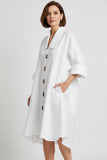 White shirtdress with brown buttons on a hanger against a plain background