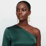 Woman wearing a green one-shoulder dress with gold earrings on a white background