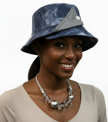 Blue tie-dye bucket hat with gray accents on a mannequin head, paired with a silver necklace.