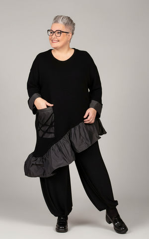 Person wearing a black outfit with ruffled layers on a beige background