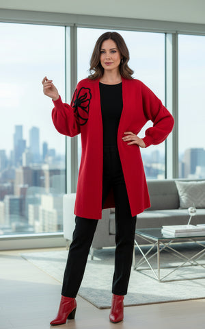 Person wearing a red cardigan with a black flower design, white pants, and beige boots on a white background