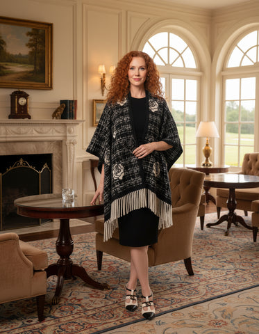 Person wearing a black and white patterned poncho with fringe on a white background