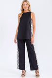 Woman wearing a black sleeveless top and pants with white trim on a white background