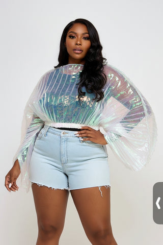 Person wearing a transparent, iridescent top with light blue shorts on a plain background