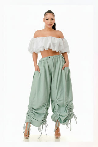 Woman wearing a white off-shoulder top and light blue ruffled pants on a white background
