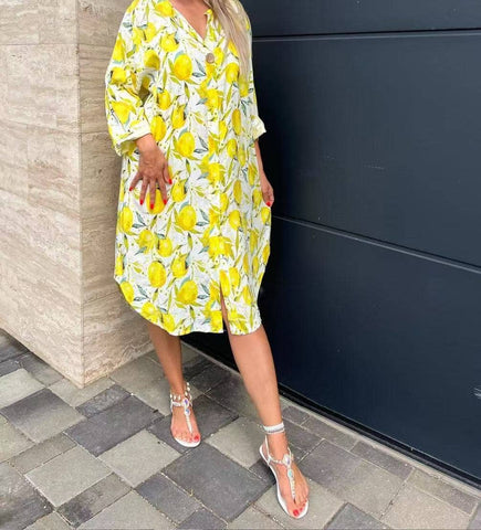 A mid-length yellow dress with lemon print, featuring a scoop neckline and 3/4 sleeves, worn by a model standing against a black background.