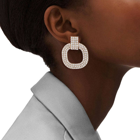 Close-up of an ear wearing a large, round, pearl-like earring with a blurred background.