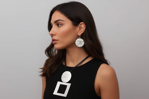 Woman wearing a black top with a silver necklace and earrings against a gray background