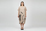 Beige dress with black abstract patterns on a hanger against a white wall