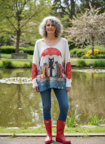 Cardigan with a colorful cat design on a hanger against a white wall