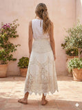 Woman wearing a white lace dress standing in front of a beige wall with potted plants.