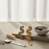 Gold earrings on a neutral surface with a bowl of stones and other jewelry items.